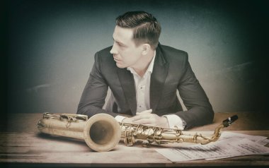 Håkon Kornstad in a suit sitting behind a saxophone and sheet music. 