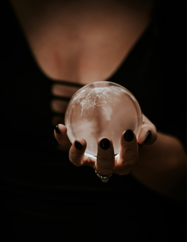 A woman's torso, dressed in black, and holding a crystal ball