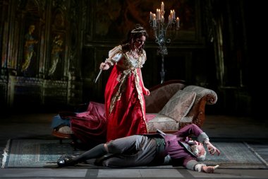 Tosca, the knife still in her hand, looms over the dying Scarpia 