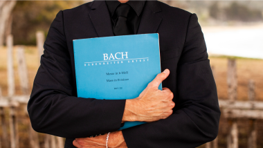 A person holds a blue book of some of Bach's works.