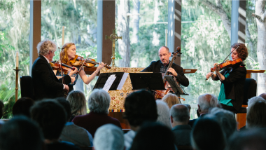 A string quartet plays for an audience in a venue in a forest.