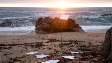 A music stand stands on an empty beach at sunset.