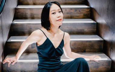Yeol Eum Son poses sitting on a staircase in a dark blue dress.