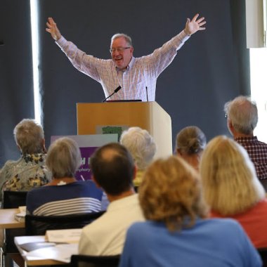 Instructor Scott Foglesong stands behind lecture stand with arms up in front of class.