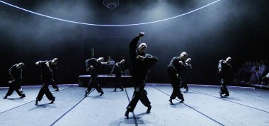 Dancers dressed in a black costume is dancing on a dark stage