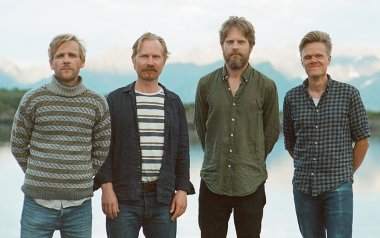 The members of the Danish String Quartet standing in front of a clear blue lake 