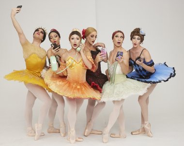 Members of the Les Ballets Trockadero de Monte Carlo in colorful ballet attire posing in front of a white backdrop