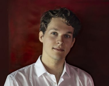 Lukas Sternath is looking into the camera and is pictured in front of a dark red background