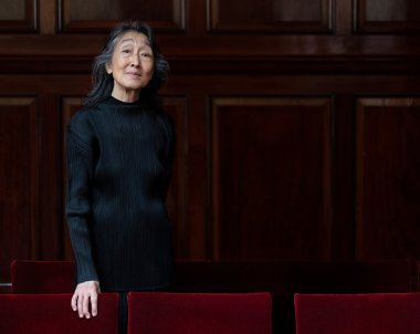 Mitsuko Uchida posing in front of a wooden wall