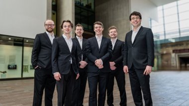Six singers posing in black suits