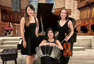 In front of grand piano, pianist and violinist (standing) and bandoneon player (seated in center)