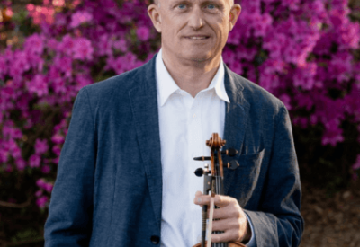 Espen Lilleslåttenen stands with his violin against a background of purple flowers