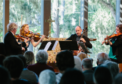 A string quartet plays for an audience in a venue in a forest.