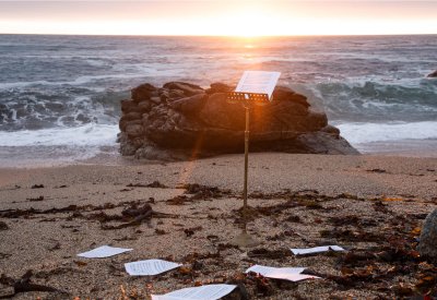 A music stand stands on an empty beach at sunset.