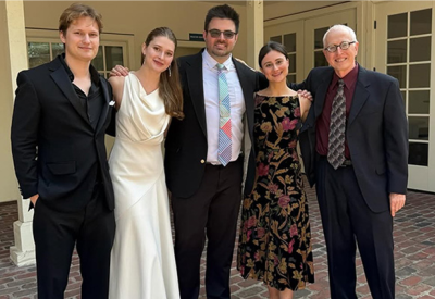 Four people stand with their arms around each other, wearing formal concert dress.