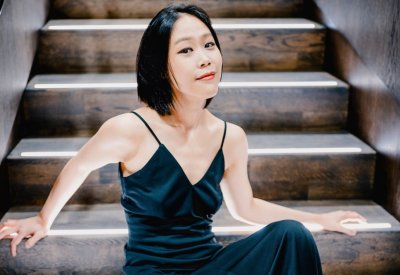 Yeol Eum Son poses sitting on a staircase in a dark blue dress.
