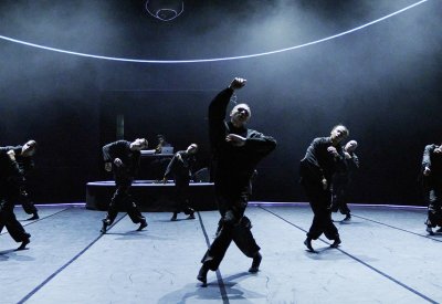 Dancers dressed in a black costume is dancing on a dark stage