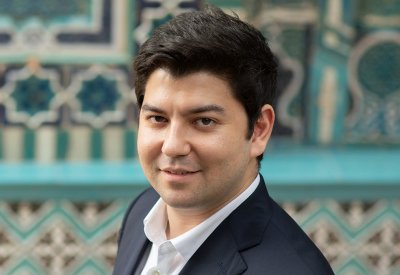 A portrait of Behzod Abdraimov in front of a blue patterned background
