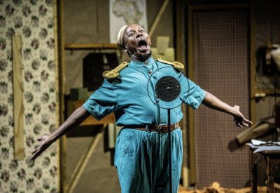 A man in a blue costume is singing in front of a microphone with his arms stretched out.