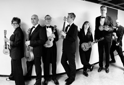 A black and white photo of the Ukulele Orchestra of Great Britain holding their ukulele 